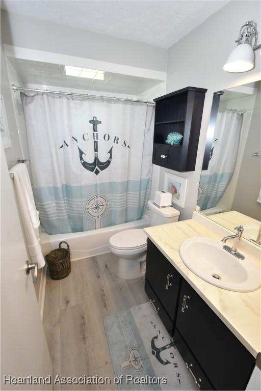 bathroom with vanity, shower / bathtub combination with curtain, toilet, and wood finished floors