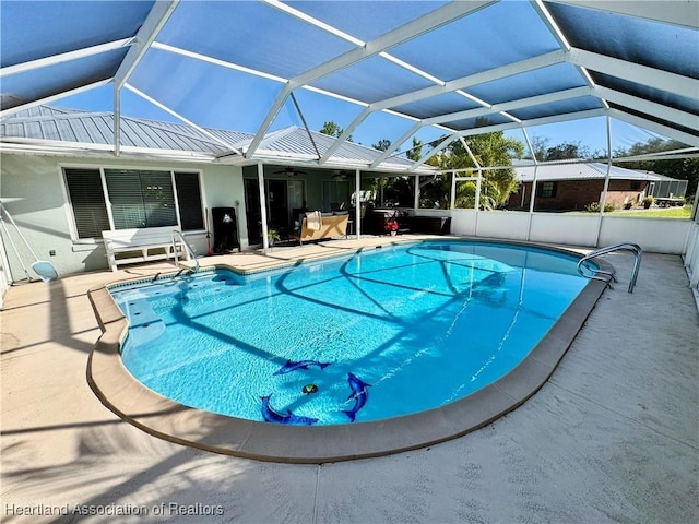 outdoor pool with glass enclosure, a ceiling fan, and a patio area