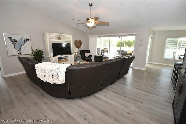 living area featuring lofted ceiling, a healthy amount of sunlight, light wood-type flooring, and ceiling fan