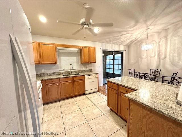 kitchen featuring pendant lighting, white appliances, ceiling fan with notable chandelier, sink, and light stone countertops