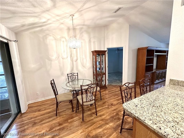 dining space featuring hardwood / wood-style floors, an inviting chandelier, and lofted ceiling