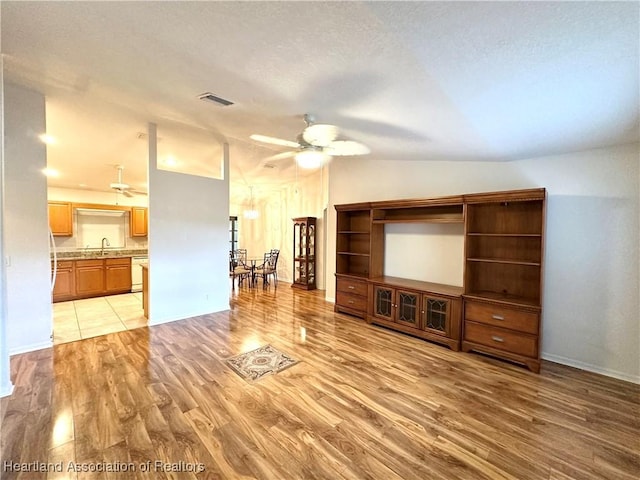 unfurnished living room featuring light hardwood / wood-style flooring, ceiling fan, lofted ceiling, and sink