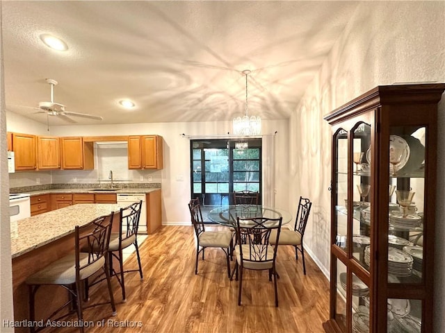 dining space with ceiling fan with notable chandelier, sink, and light hardwood / wood-style flooring