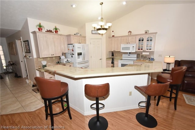 kitchen with a breakfast bar, white appliances, kitchen peninsula, and vaulted ceiling