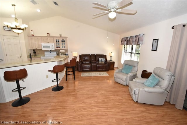 living room with ceiling fan with notable chandelier, light hardwood / wood-style floors, and vaulted ceiling