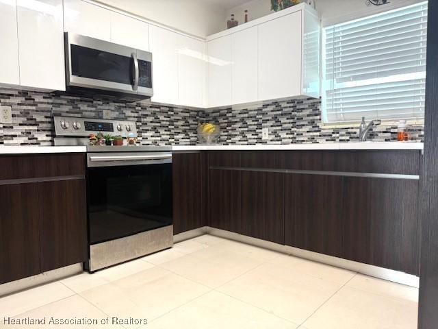 9590 NW 22nd Ave, Miami, FL 33147 - kitchen featuring dark brown cabinetry, stainless steel appliances, white cabinetry, light countertops, and modern cabinets