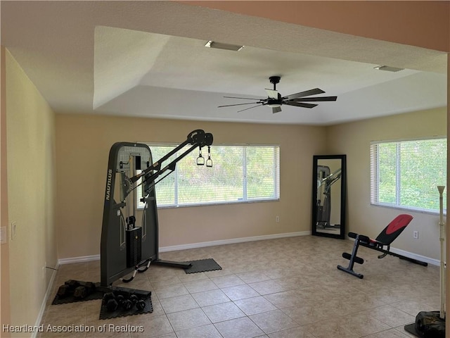 workout area with light tile patterned floors, a tray ceiling, and ceiling fan