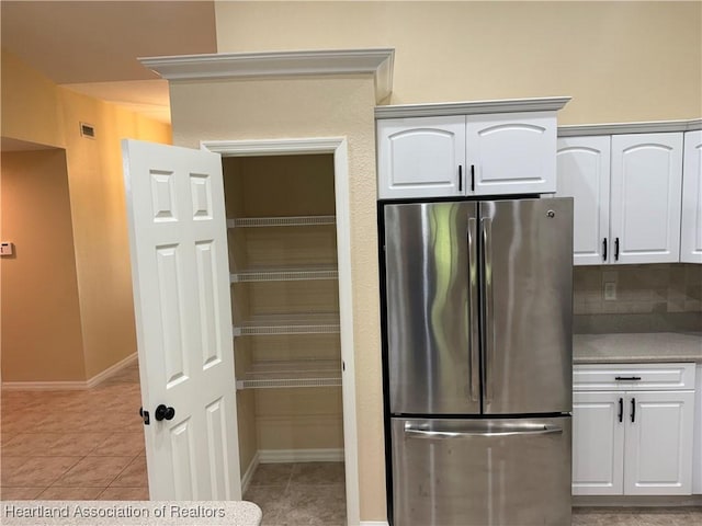 kitchen with light tile patterned floors, white cabinetry, stainless steel refrigerator, and tasteful backsplash