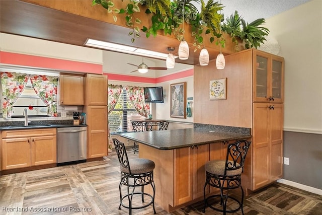 kitchen featuring ceiling fan, sink, stainless steel dishwasher, a kitchen bar, and light wood-type flooring