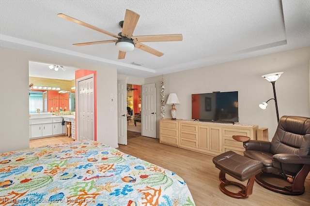 bedroom with ensuite bath, ceiling fan, light hardwood / wood-style floors, a tray ceiling, and a closet