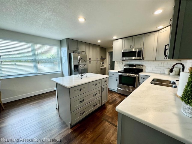 kitchen with gray cabinetry, sink, dark hardwood / wood-style floors, a kitchen island, and appliances with stainless steel finishes