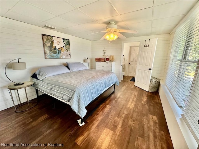 bedroom featuring a paneled ceiling, ceiling fan, dark wood-type flooring, and wooden walls