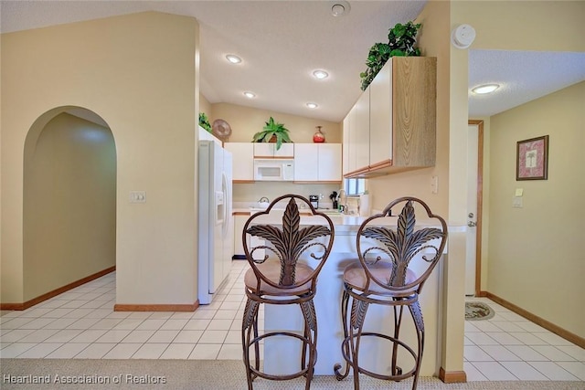 kitchen with lofted ceiling, white appliances, and light tile patterned floors