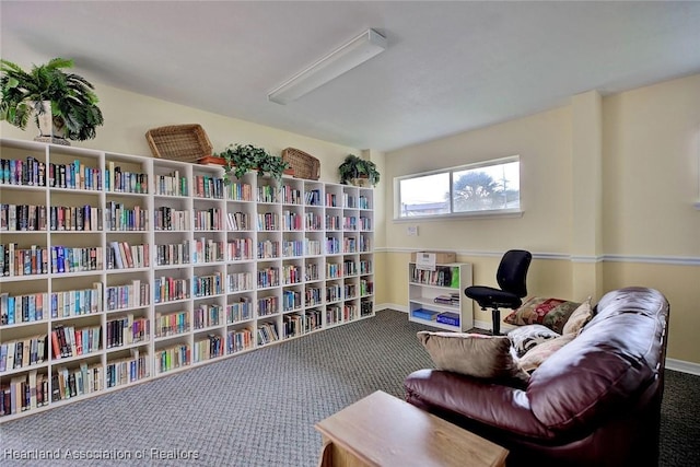 sitting room featuring carpet flooring, wall of books, and baseboards