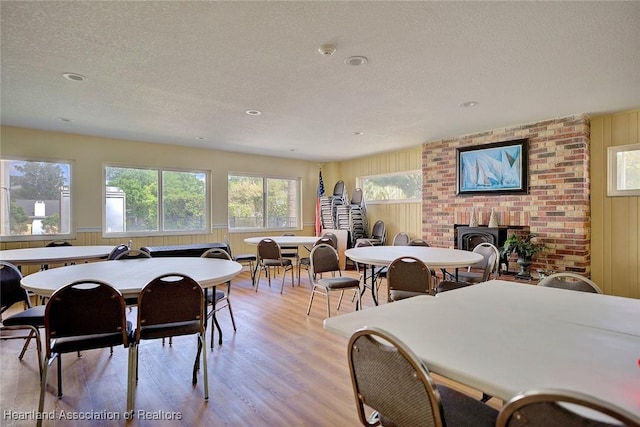 dining room with light wood-type flooring, wood walls, and a textured ceiling