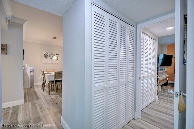 hall featuring a textured ceiling, ornamental molding, wood finished floors, and baseboards