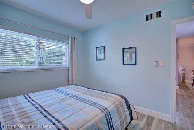 bedroom with a ceiling fan, visible vents, baseboards, and wood finished floors