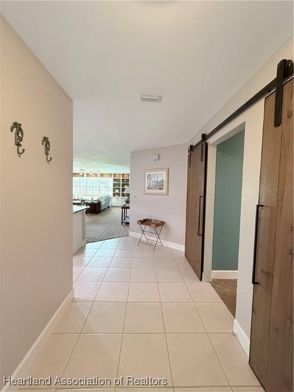 hallway with light tile patterned floors, a barn door, visible vents, and baseboards