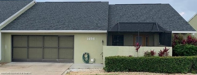 view of front of property with driveway, roof with shingles, an attached garage, and stucco siding