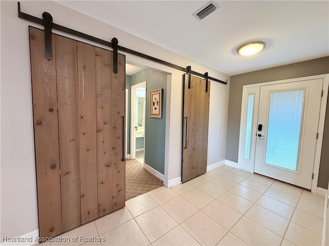 foyer entrance featuring light tile patterned floors, a barn door, visible vents, and baseboards