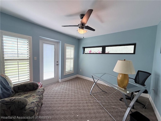 carpeted office space with a ceiling fan and baseboards