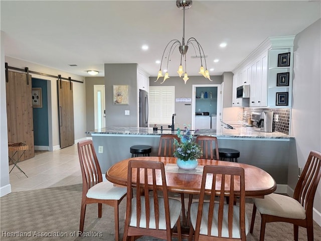 dining space featuring washing machine and clothes dryer, light tile patterned floors, recessed lighting, a barn door, and a chandelier