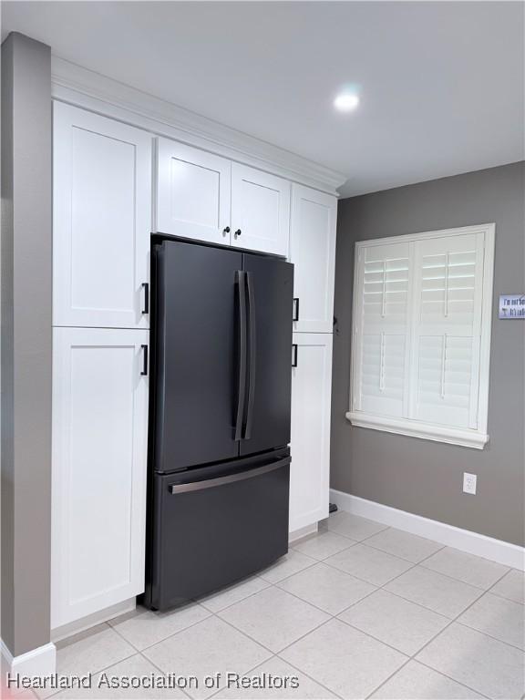 kitchen with light tile patterned floors, baseboards, freestanding refrigerator, and white cabinetry