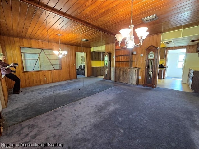 interior space with an inviting chandelier, wood walls, and dark colored carpet