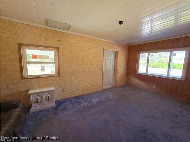 unfurnished living room featuring crown molding, brick wall, wooden walls, and dark carpet