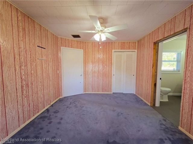 unfurnished bedroom featuring connected bathroom, wood walls, ceiling fan, and carpet