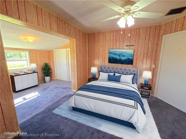 carpeted bedroom featuring ceiling fan and wood walls