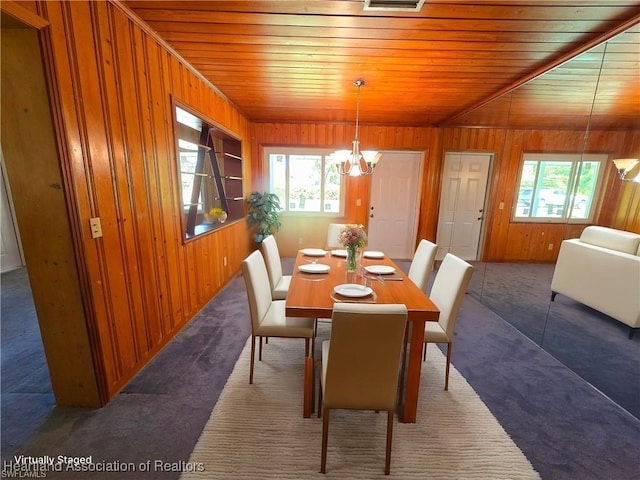 carpeted dining area featuring wooden walls, wooden ceiling, and a chandelier