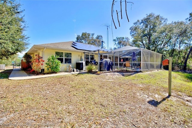 rear view of property with a yard, a lanai, and solar panels