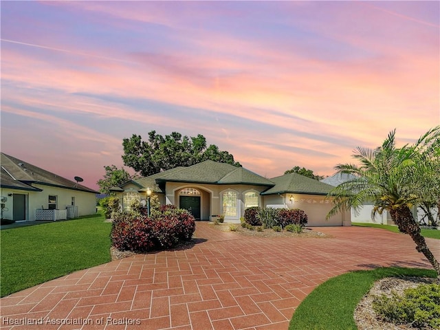 view of front facade with an attached garage, a front lawn, stucco siding, and decorative driveway