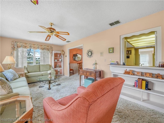 living area featuring ceiling fan, a textured ceiling, carpet, and visible vents