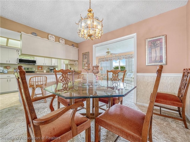 dining area with a wainscoted wall, light carpet, a textured ceiling, and ceiling fan with notable chandelier