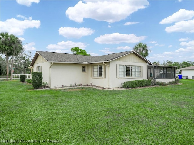 rear view of property with a sunroom, roof with shingles, and a yard