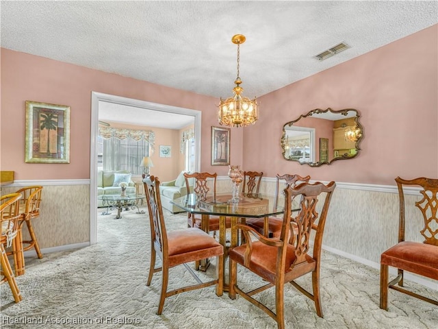 dining room with visible vents, a wainscoted wall, light carpet, and a textured ceiling