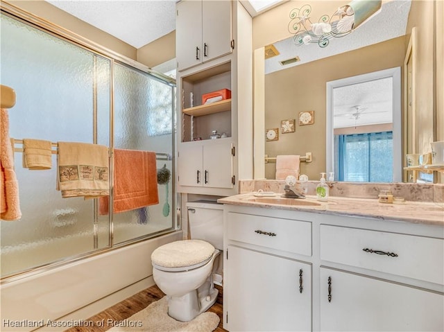 bathroom with bath / shower combo with glass door, toilet, ceiling fan, wood finished floors, and vanity