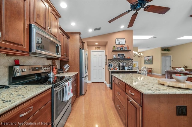 kitchen with lofted ceiling, tasteful backsplash, light stone counters, appliances with stainless steel finishes, and light hardwood / wood-style floors