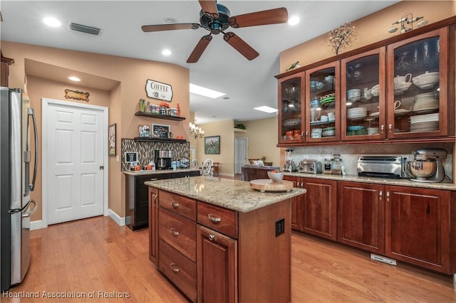 kitchen featuring a kitchen island, ceiling fan, stainless steel refrigerator with ice dispenser, light stone countertops, and light wood-type flooring