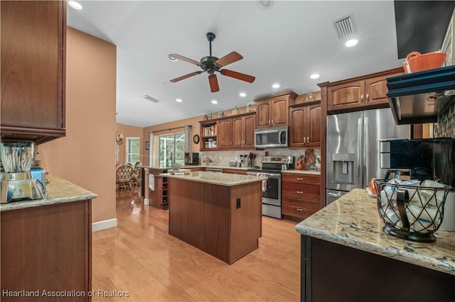 kitchen with a kitchen island, appliances with stainless steel finishes, tasteful backsplash, light stone countertops, and light wood-type flooring