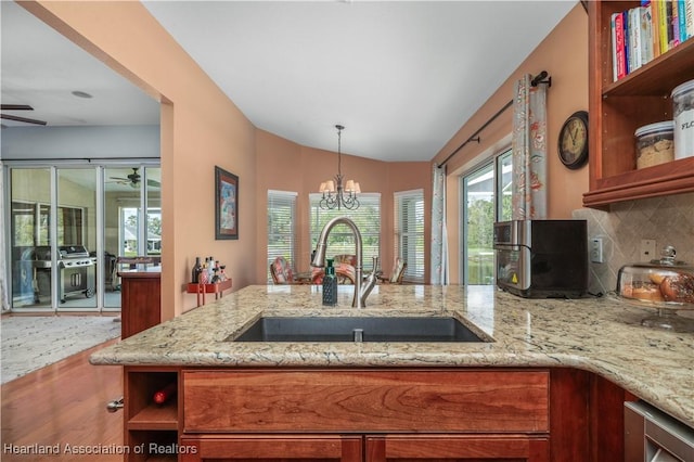 kitchen featuring hanging light fixtures, light stone countertops, sink, and ceiling fan with notable chandelier