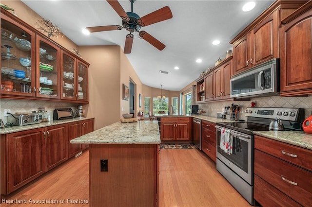 kitchen with light hardwood / wood-style flooring, stainless steel appliances, light stone counters, a kitchen island, and decorative light fixtures