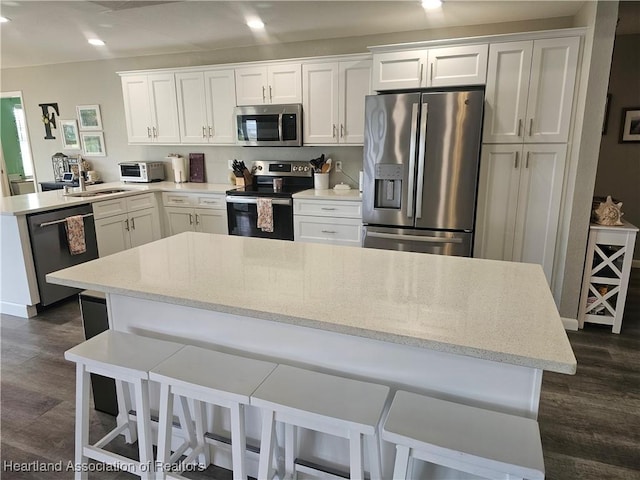 kitchen featuring white cabinetry, a kitchen bar, appliances with stainless steel finishes, dark hardwood / wood-style flooring, and a center island