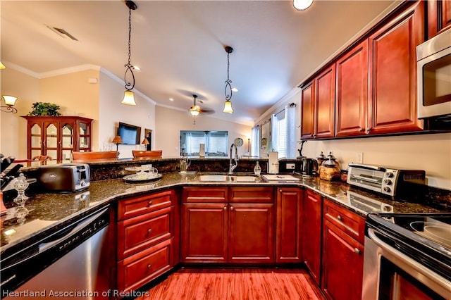 kitchen featuring appliances with stainless steel finishes, dark stone counters, vaulted ceiling, sink, and decorative light fixtures