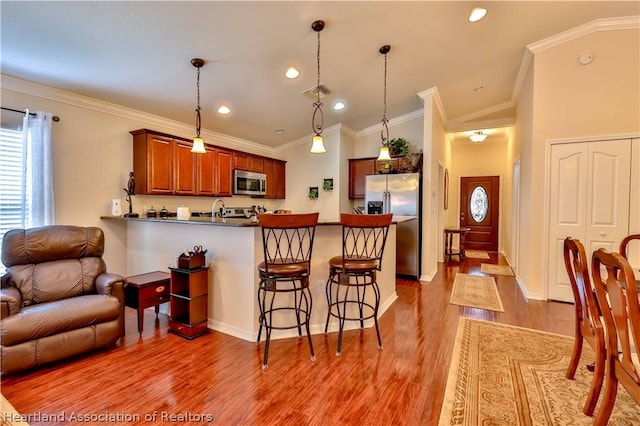 kitchen with kitchen peninsula, pendant lighting, stainless steel appliances, and wood-type flooring