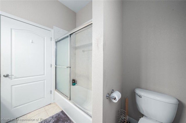 bathroom with tile patterned floors, toilet, and bath / shower combo with glass door