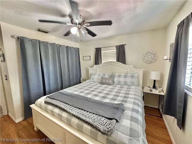 bedroom featuring a ceiling fan, baseboards, visible vents, and wood finished floors