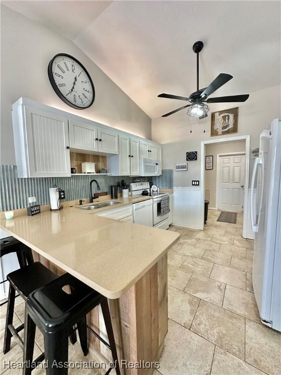 kitchen featuring a peninsula, white appliances, a sink, light countertops, and a kitchen bar